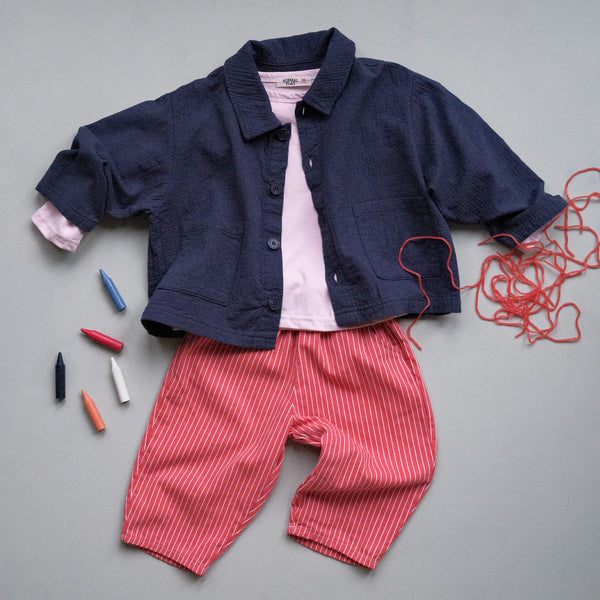 Children's outfit with navy jacket, pink shirt, red striped pants, and colorful crayons on a gray background