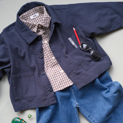 Navy jacket, brown check shirt, and blue barrel jeans on a light gray surface with small toys.