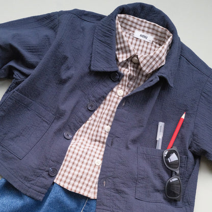 Navy blue  chore jacket with plaid brown shirt, sunglasses, and red pen on a light gray background