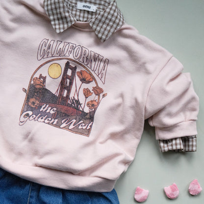 Pink sweatshirt with 'California, THE GOLDEN WEST' graphic design, brown check shirt and blue jeans